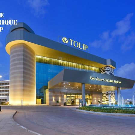 Tolip Resort El Galala Majestic Ain Sukhna Bagian luar foto The photo shows a modern hotel building named "Tolip Resort & Spa," featuring a sleek architectural design with large glass windows. The hotel is illuminated against a twilight sky, showcasing its prominent signage. In the foreground, there is a well