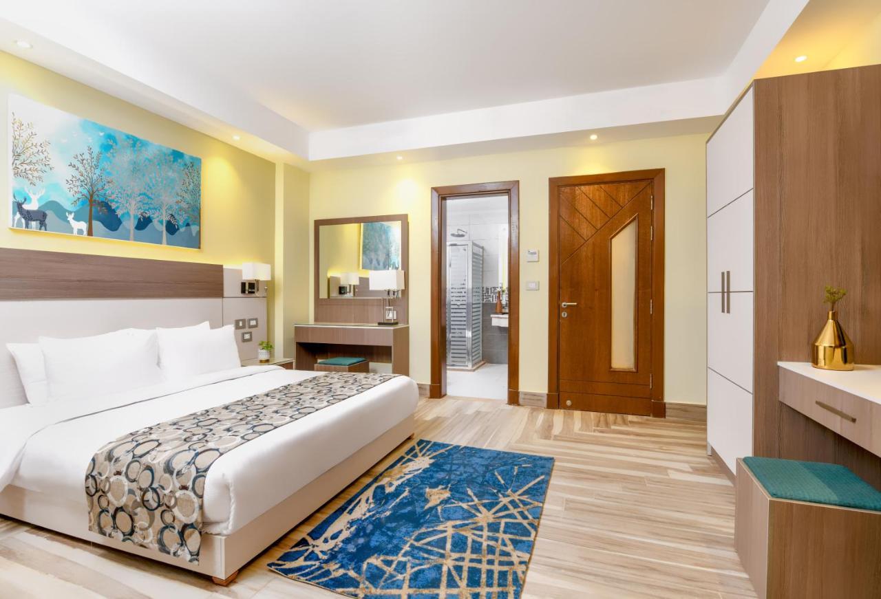 Tolip Resort El Galala Majestic Ain Sukhna Bagian luar foto The photo shows a well-decorated hotel room. There is a large bed with white linens and a decorative throw blanket. The room features a wooden wardrobe and a bedside table with lamps. A colorful rug is placed on the floor, adding warmth to the space.