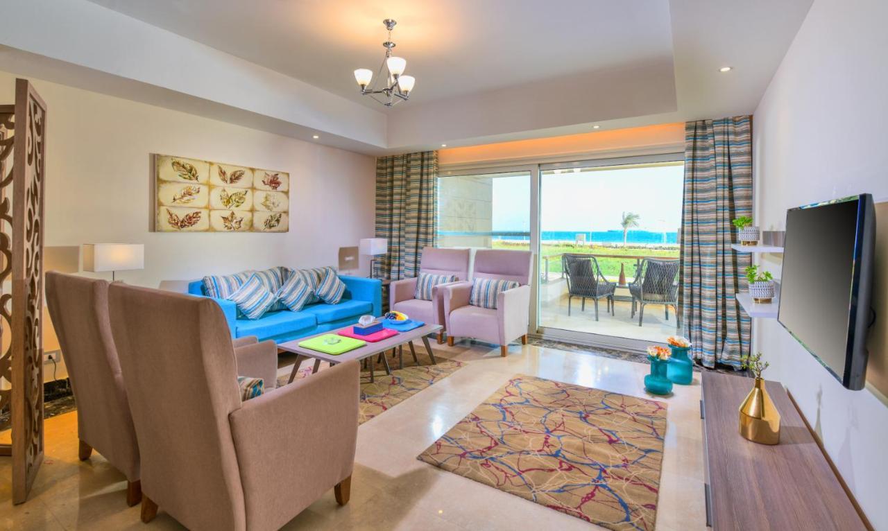 Tolip Resort El Galala Majestic Ain Sukhna Bagian luar foto The photo shows a bright and modern living room. It features a blue sofa with decorative cushions, two light-colored armchairs, and a coffee table. A large area rug adds warmth to the space, which is decorated with a subtle pattern. The walls have so