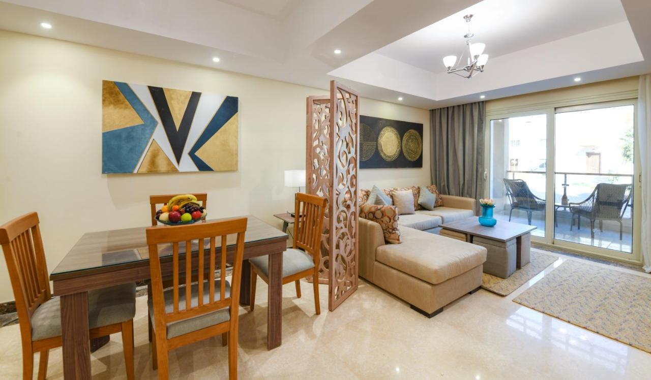 Tolip Resort El Galala Majestic Ain Sukhna Bagian luar foto The photo shows a modern and stylish interior of a living space. It features a seating area with a plush sofa and decorative cushions, complemented by a wooden coffee table. There is a dining table with wooden chairs nearby. 

On the walls, there are
