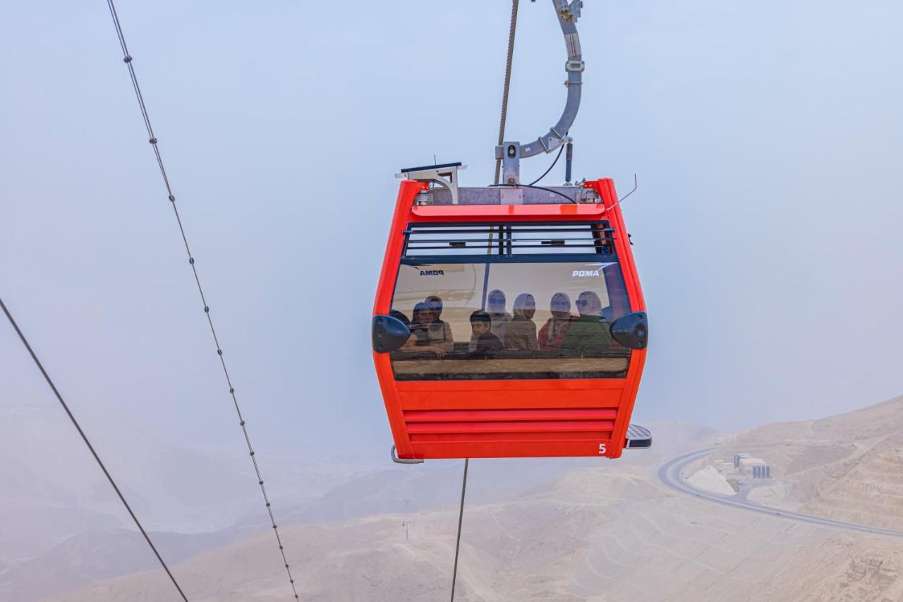 Tolip Resort El Galala Majestic Ain Sukhna Bagian luar foto The photo shows a red gondola lift suspended in the air, traveling along cables. Inside the gondola, a group of people can be seen. The background features a hazy landscape, possibly mountains or hills, indicating an elevated area. The scene conveys 