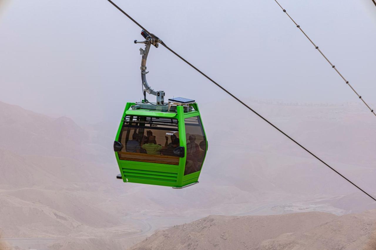 Tolip Resort El Galala Majestic Ain Sukhna Bagian luar foto The photo shows a green cable car suspended in the air, moving along a wire. The cable car appears to be traversing a mountainous landscape, which looks rocky and arid. The surrounding environment is somewhat foggy or hazy, suggesting limited visibil