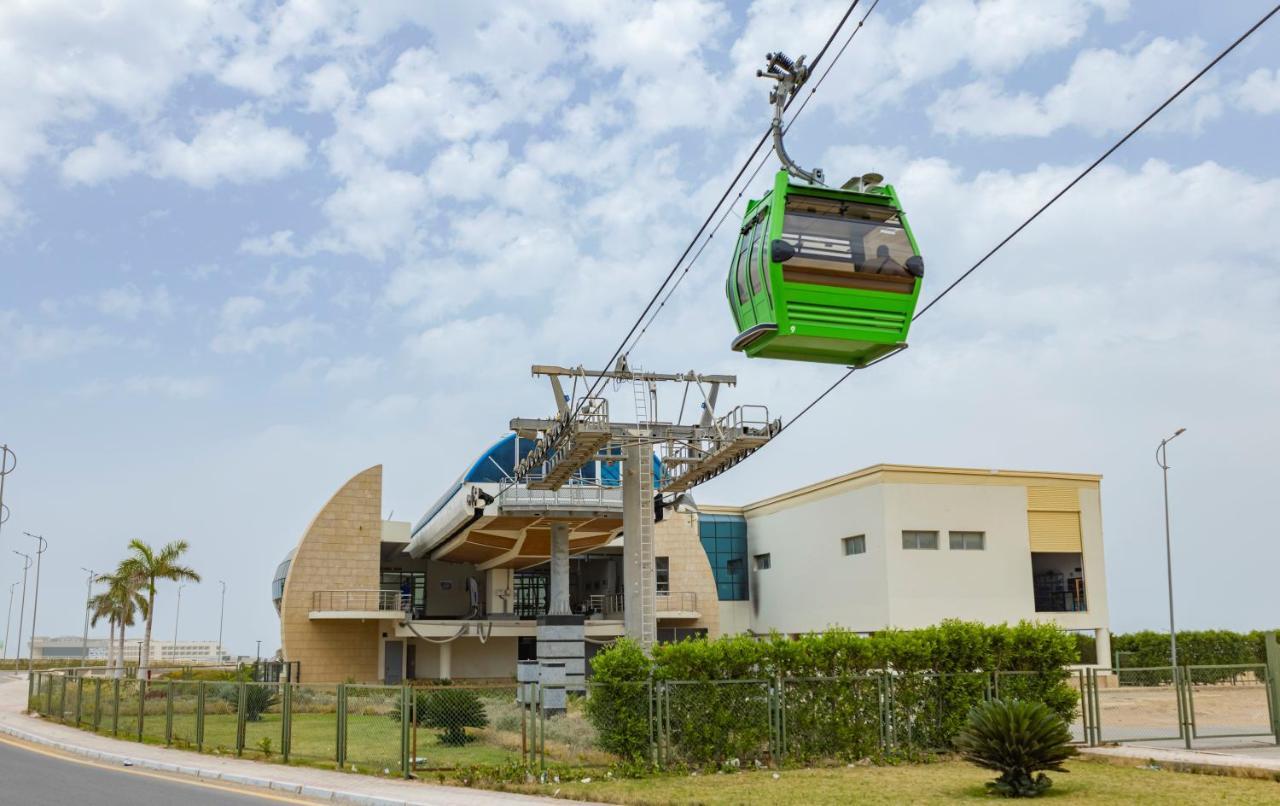 Tolip Resort El Galala Majestic Ain Sukhna Bagian luar foto The photo shows a cable car or gondola system in operation, featuring a green-colored gondola. It is suspended from cables and moving towards a station, which appears to be a modern building with a unique architectural design. The station has large w
