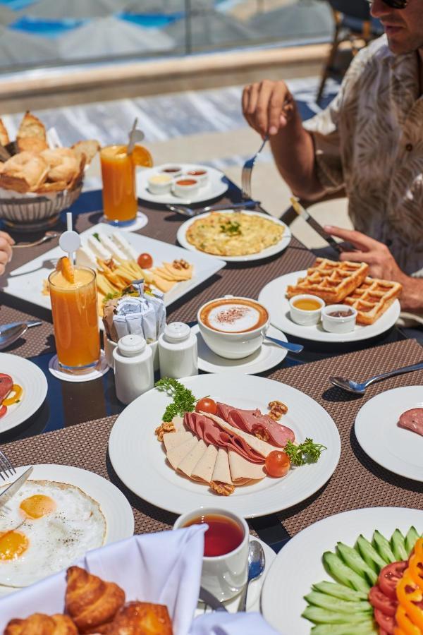 Tolip Resort El Galala Majestic Ain Sukhna Bagian luar foto The photo shows a breakfast spread laid out on a table. There are several plates with a variety of food items, including:

1. **Sliced Cold Cuts**: A plate featuring various cold meats, accompanied by garnishes like cherry tomatoes and lettuce.
2. **