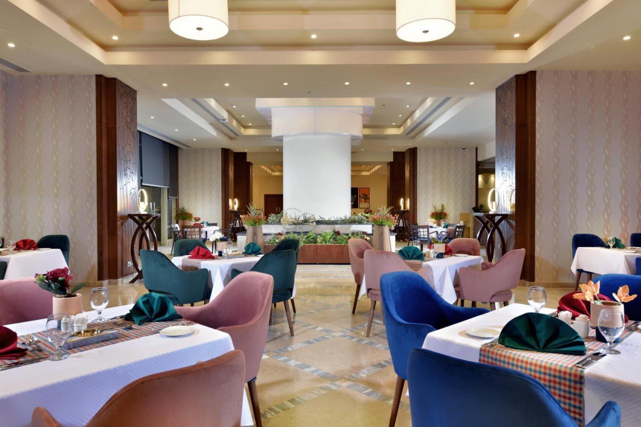 Tolip Resort El Galala Majestic Ain Sukhna Bagian luar foto The photo shows a spacious and elegantly designed restaurant interior. The layout includes several round tables dressed in white tablecloths, each set with decorative plates, cutlery, and colorful napkins. The chairs are upholstered in a variety of c